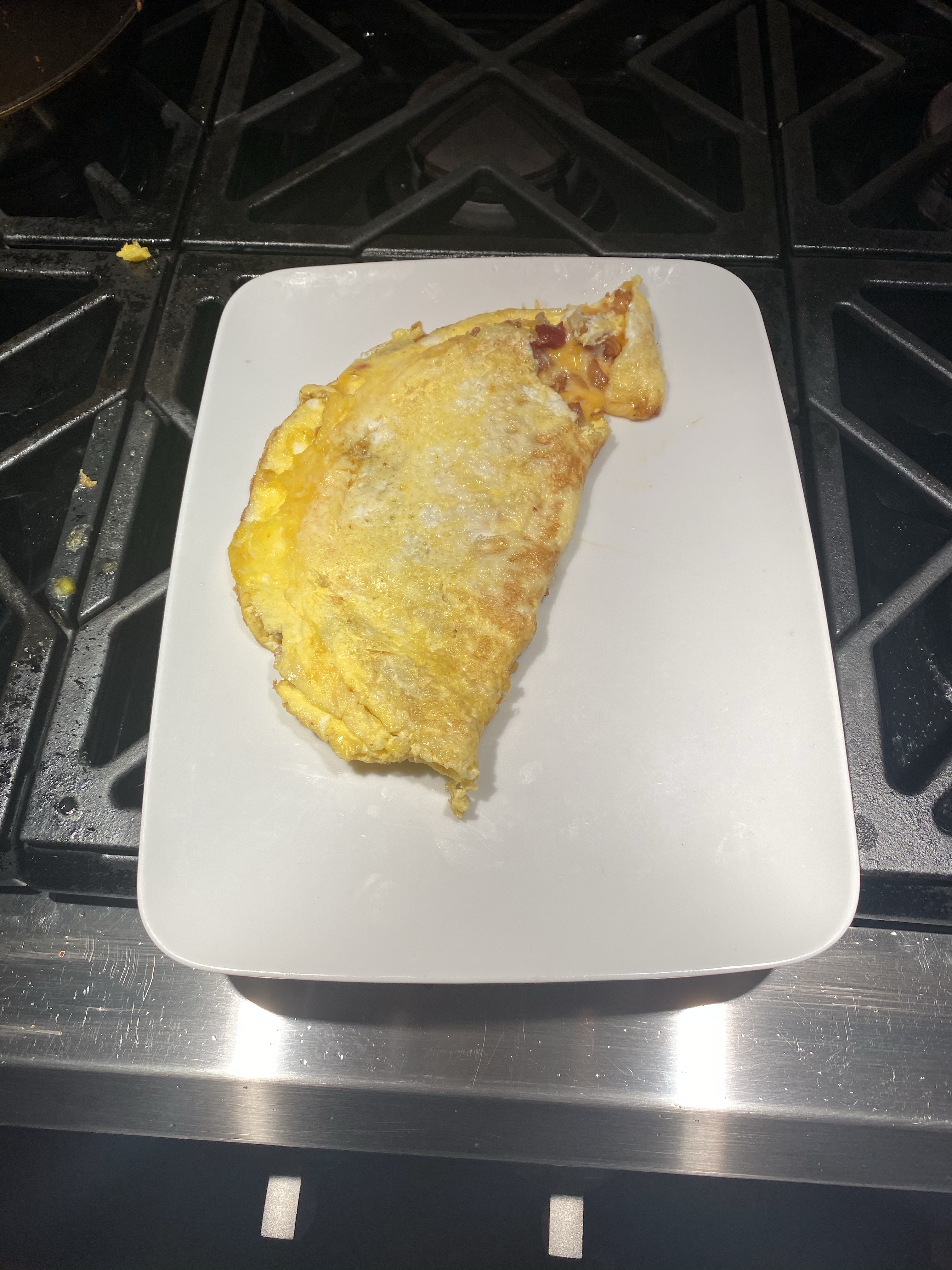 A large folded omelet on a white rectangular plate which is situated on a stovetop.